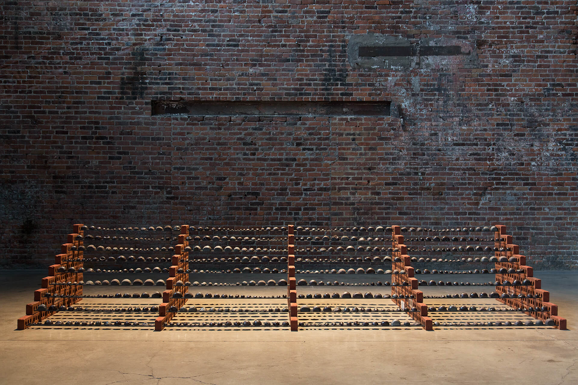 Installation view of large sculpture in a large room with a brick wall in the background.