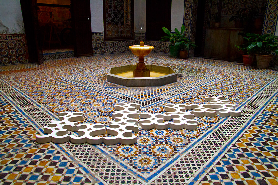 White sculptures lying on a mosaic ground next to a water fountain.
