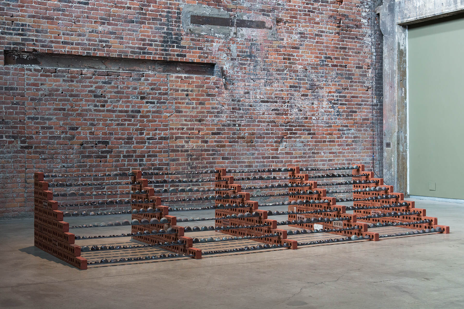 Installation view of large sculpture in a large room with a brick wall in the background.