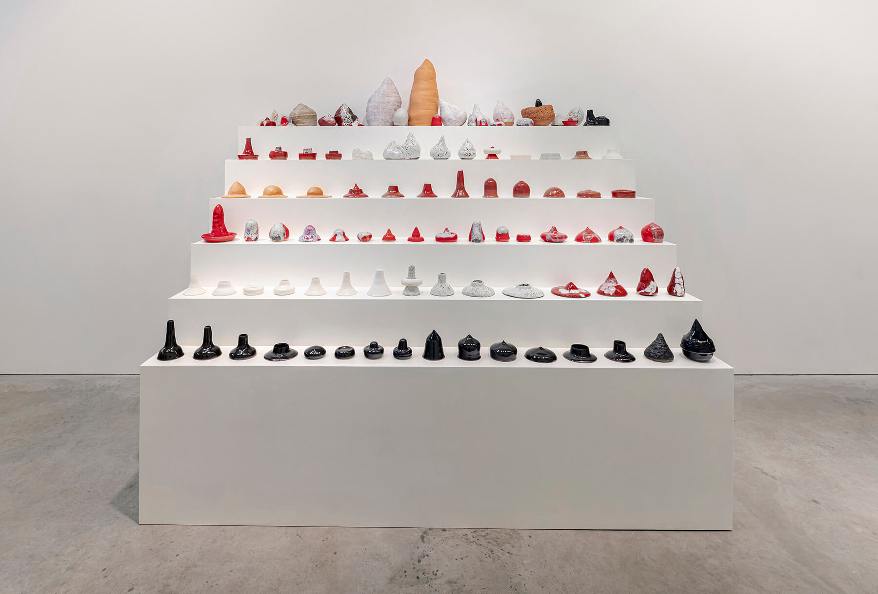 Full installation view of all sculptures lined up on a six level white plinth shaped like stair steps (front).