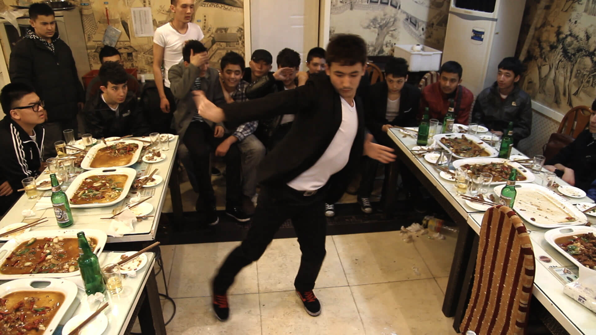 A man mid dance between two dining tables as spectators look on behind him.