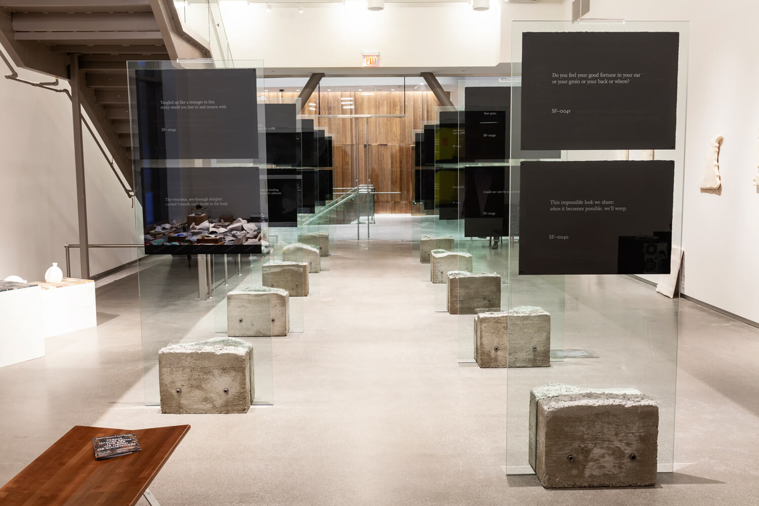 Two rows of glass panels lined up in a gallery room, each displaying two prints of white text on black paper.
