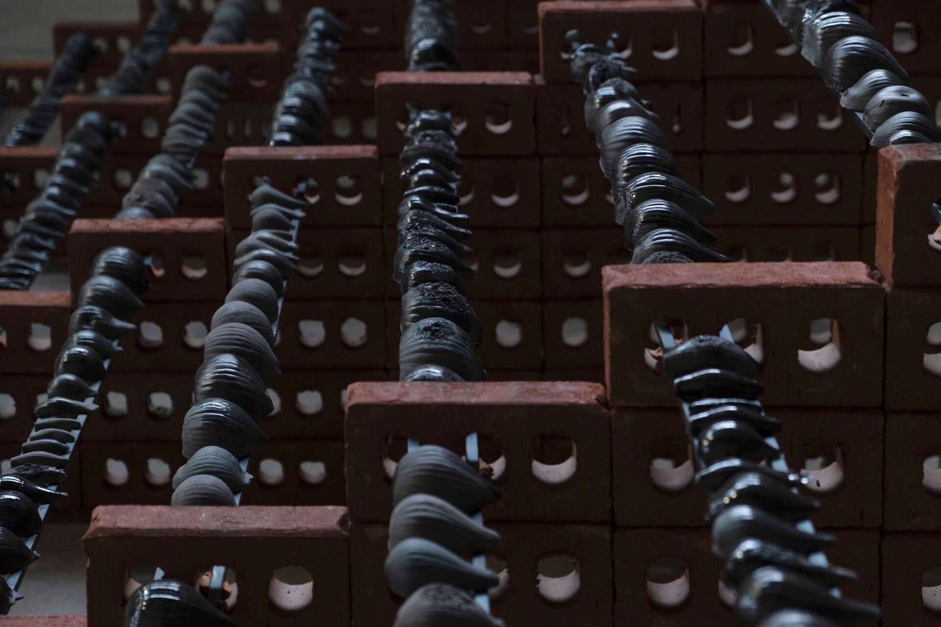 Close up view of sculpture, steel poles lined with black ceramic onions running through several half-walls made of bricks
