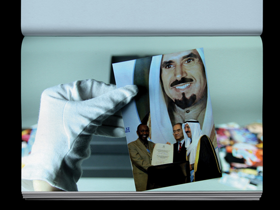 A hand wearing a white archive glove holds a photograph of three people posing for a photograph with a large portrait behind them.
