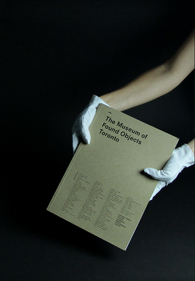 Hands wearing white archiving gloves holding the publication in front of a black background.