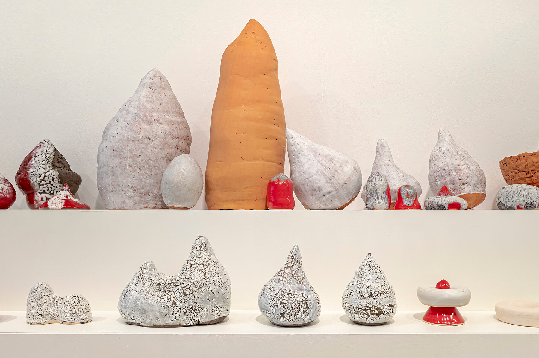 Red, white and terracotta sculptures of various shapes and sizes lined up on a two level plinth.