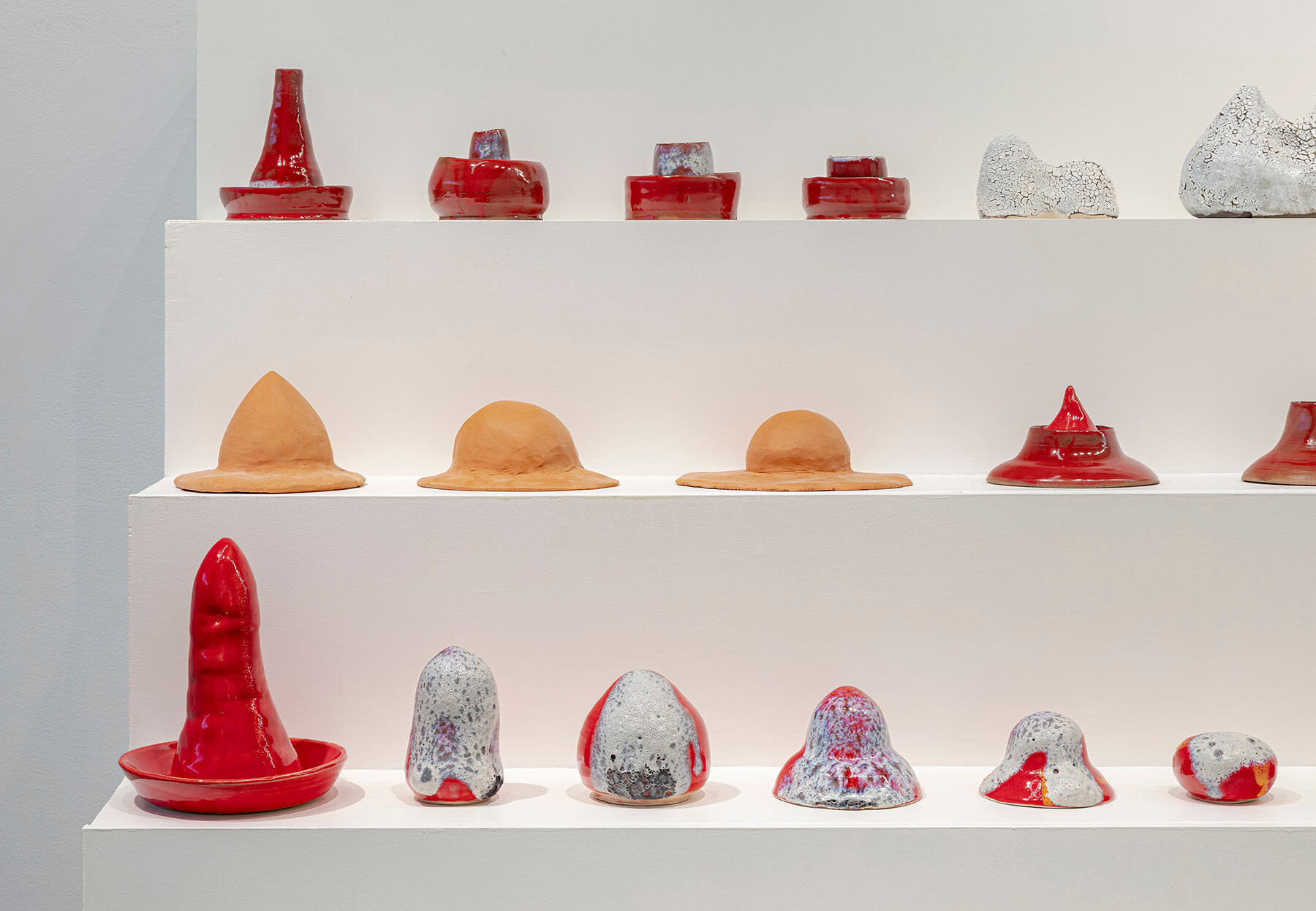 Red, white and terracotta sculptures of various shapes and sizes lined up on a three level plinth.