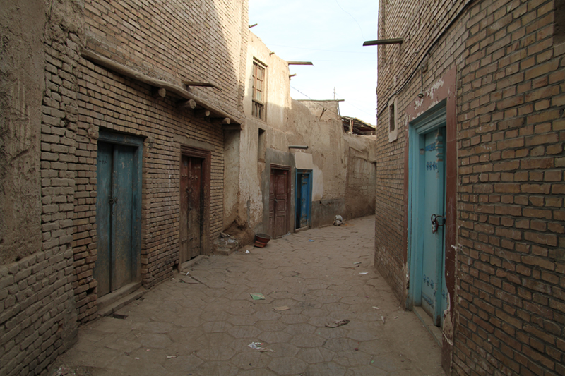 A photograph on ground level between two brick buildings with turquoise doors.