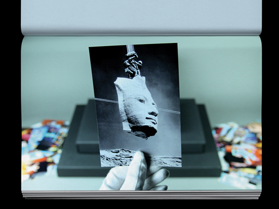 A hand wearing a white archive glove holds a black and white photograph of the face of a large sculpture removed from the body.