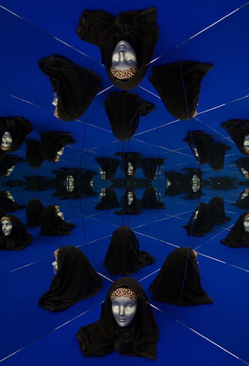 A blue display case with mirrored walls creating an optical illusion of a mannequin head wearing a leopard print bandana and a black headscarf.