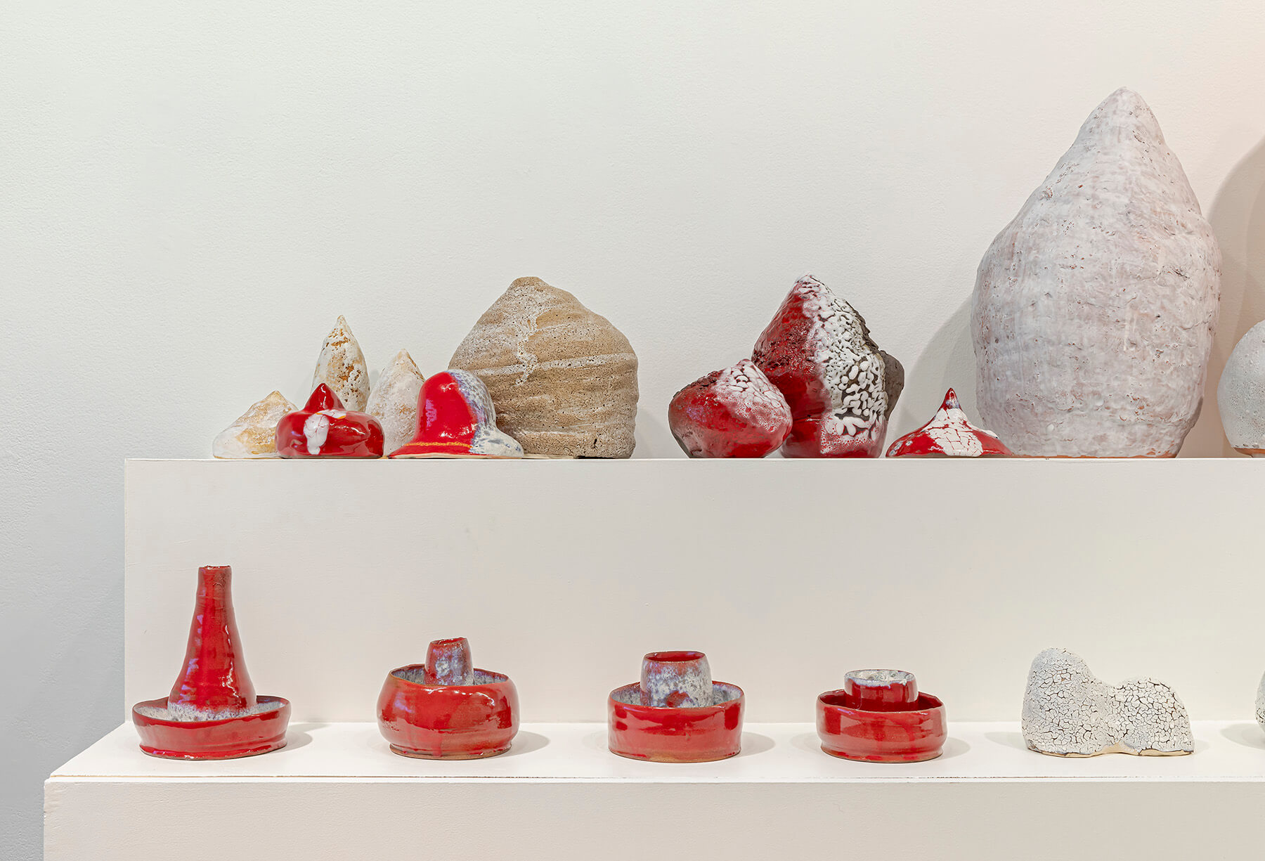 White and red sculptures of various shapes and sizes lined up on a two level plinth.