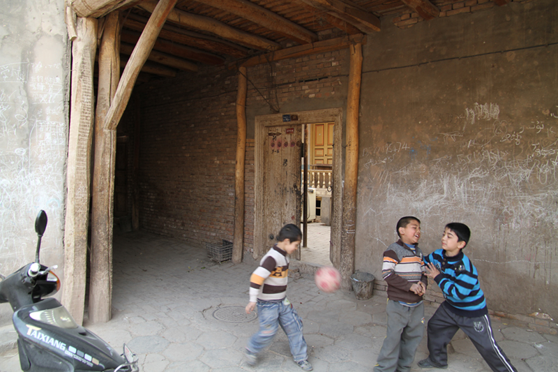 Three children playing with a soccer ball on the streets of Kashgar.