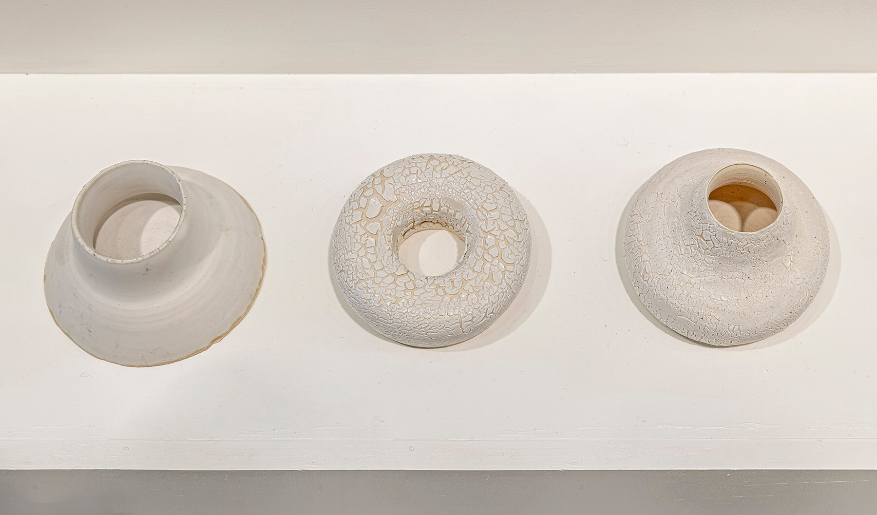 Three white sculptures of different shapes lined up on a plinth.