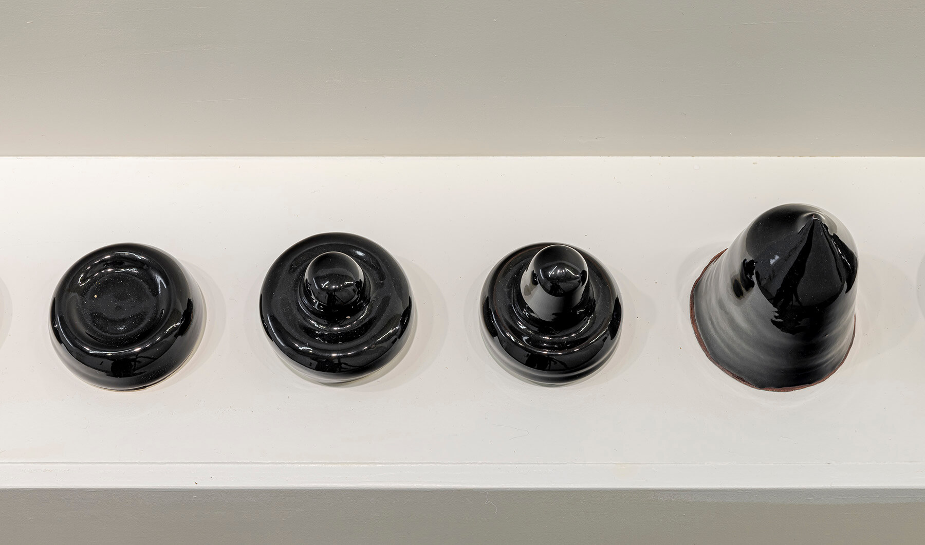 Four black sculptures of different shapes lined up on a plinth.
