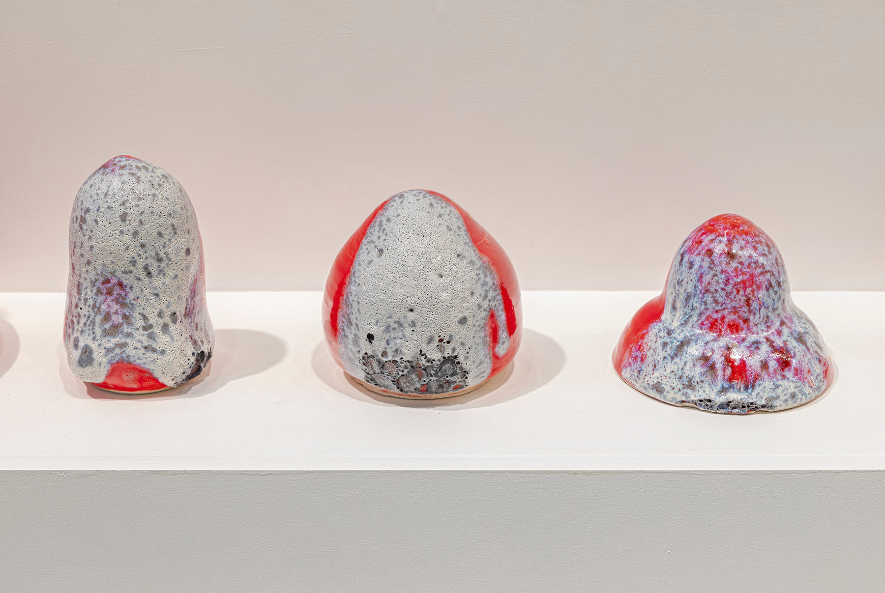 Three red and grey sculptures of different shapes lined up on a plinth.