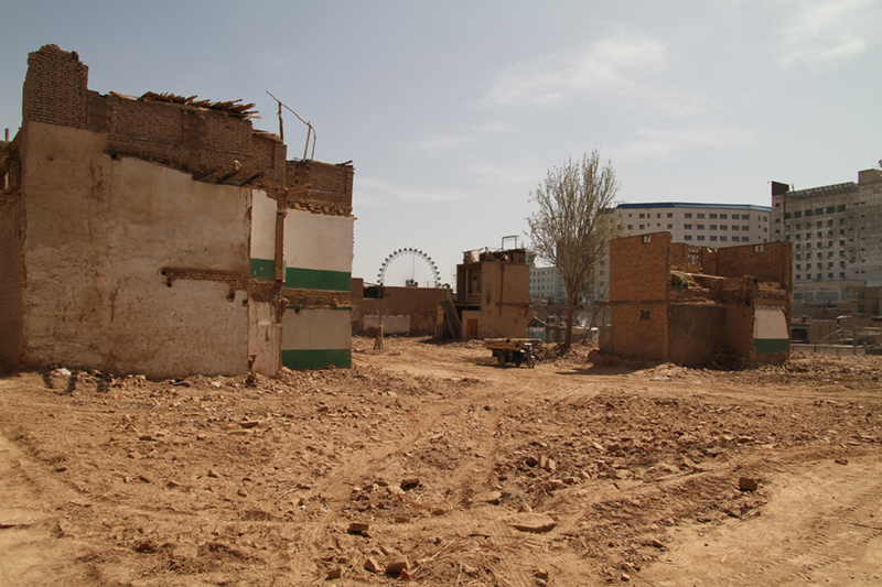 A photograph of buildings mid demolition, with a ferris wheel in the background.