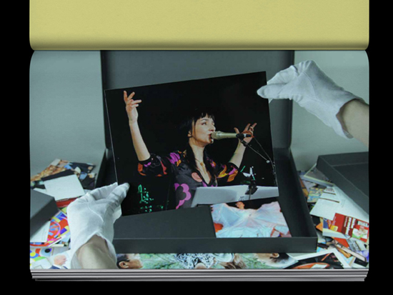 Hands wearing white archive gloves holding a photograph of a person making hand gestures speaking into a microphone.