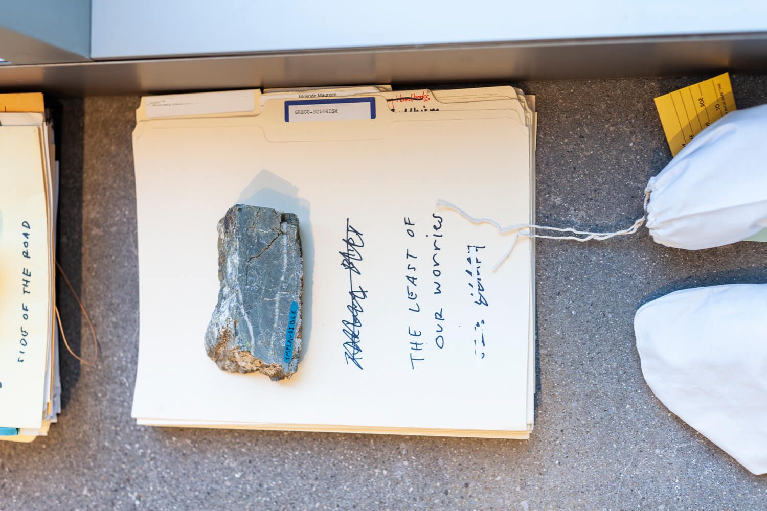Stack of file folders on the ground with a piece of stone placed on top of them, and small drawstring bags next to them.