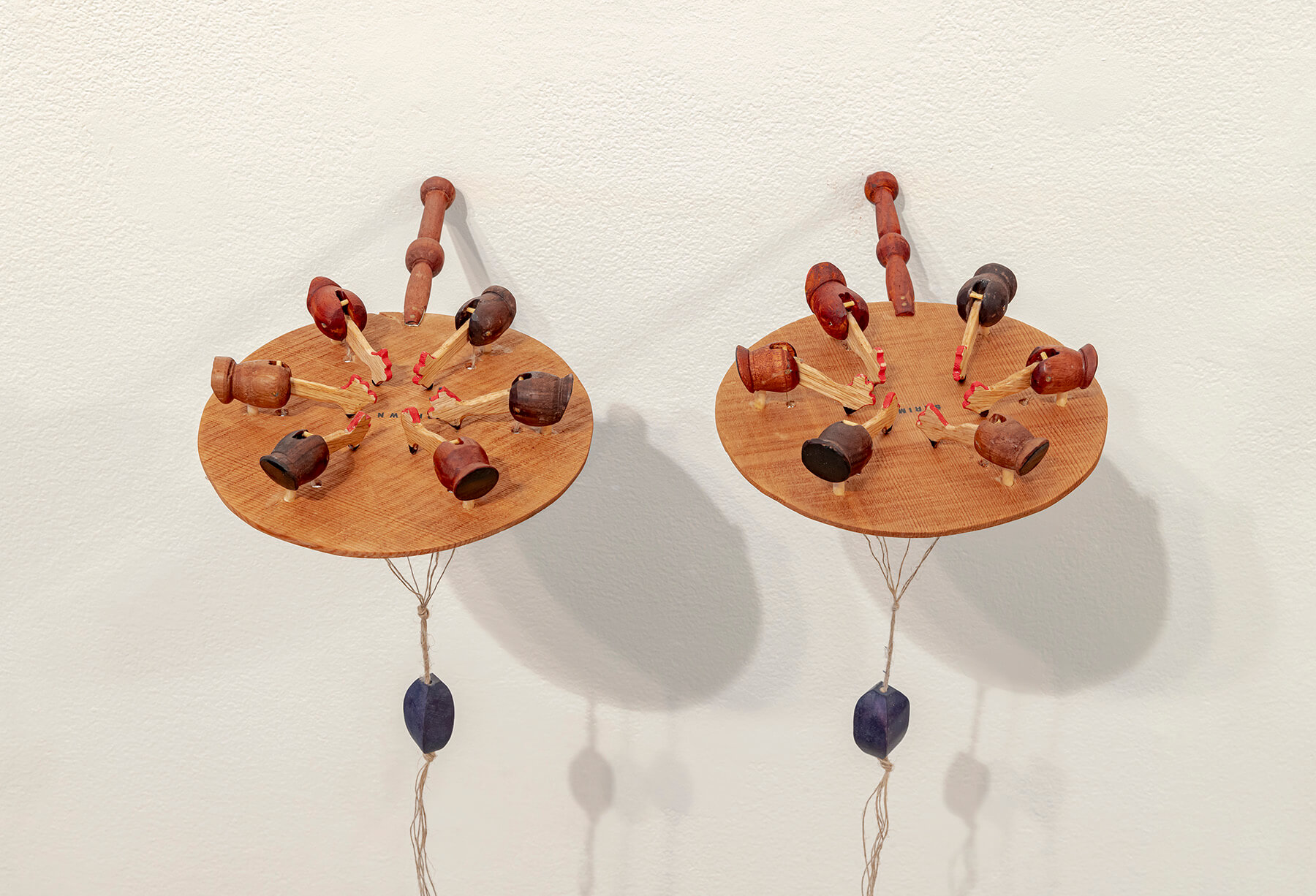 Two wooden sculptures hanging beside each other on a white wall.
