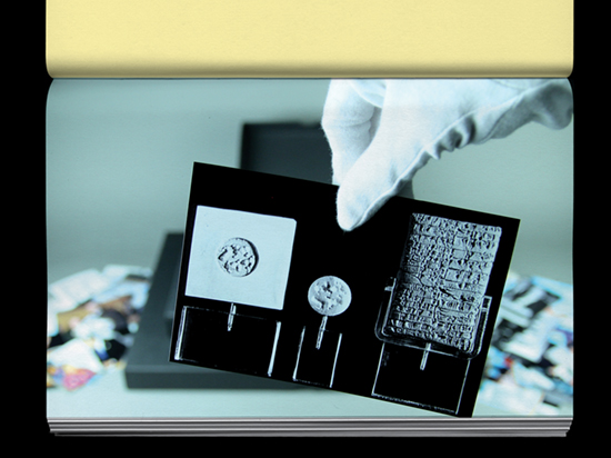 A hand wearing a white archive glove holds a photograph of a display of historic tablets.