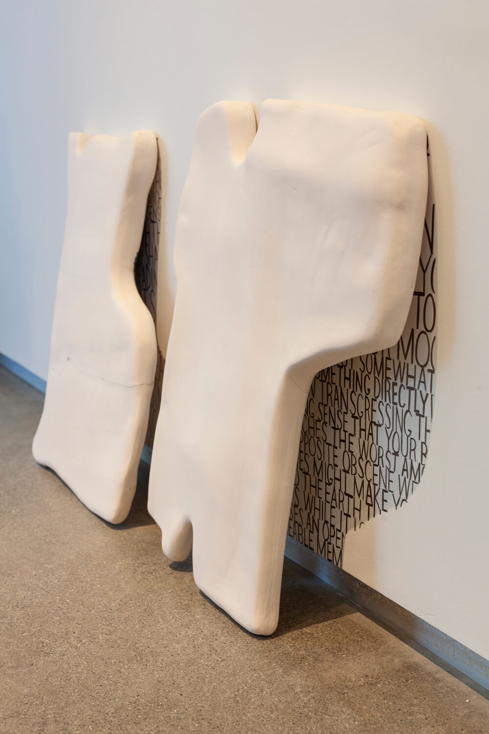 Two large tablets on the ground leaning against a wall, they cast shadows on top of black text written on the wall to fit the exact area of the shadow.